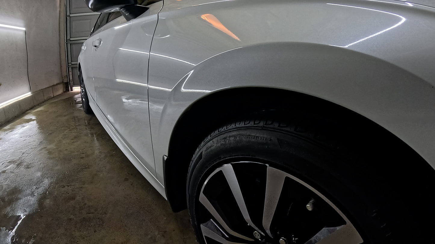 Low-angle shot from the wheel, showcasing the white car from a unique perspective, highlighting its glossy finish after paint correction and graphene ceramic coating.