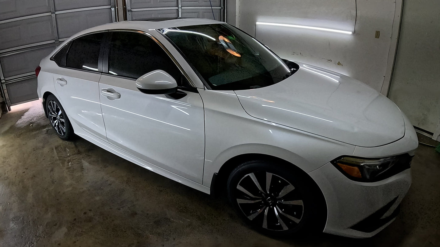 Exterior of the vehicle after paint correction, graphene ceramic coating, and window tinting, showcasing a flawless, glossy finish with the dark tint reflecting off the white surface